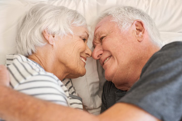 Devoted senior couple smiling warmly at each other in bed