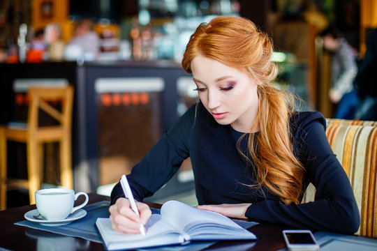 Confident young woman in smart casual wear concentrated on work while sitting in cafe