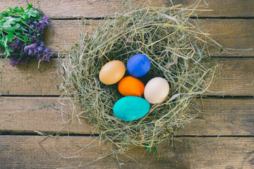 Multi-colored Easter eggs on a wooden background in the nest.