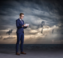 Businessman with computer tablet standing on a dark, dramatic ocean background. Business concept.