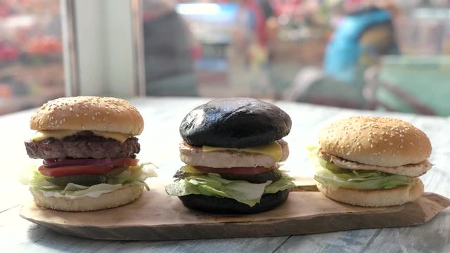 Three burgers and wooden board. Fast food on cafe table.