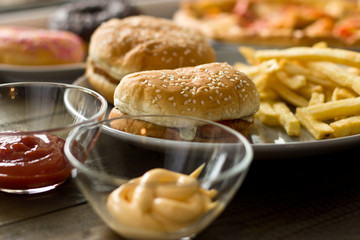 Unhealthy concept. unhealthy food: Burger, sauce, potatoes, donuts, pizza.