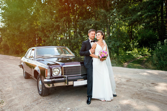 Happy newlyweds stand near the car, in the woods.