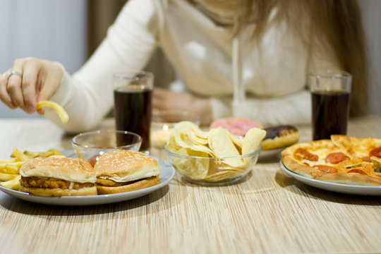 The girl is sitting at the table and eating fast food.
