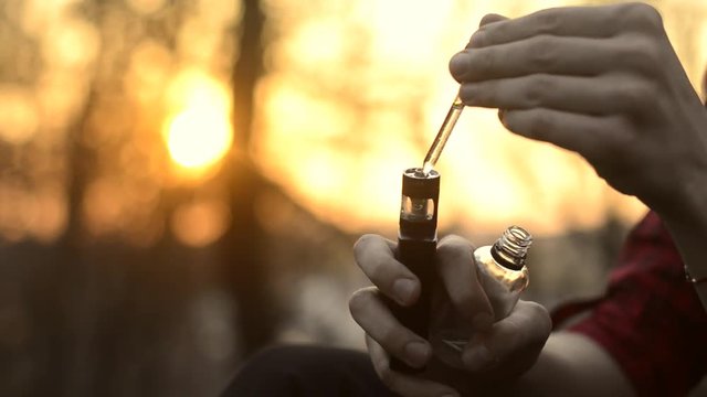 The guy pours liquid into the electronic cigarette and smokes