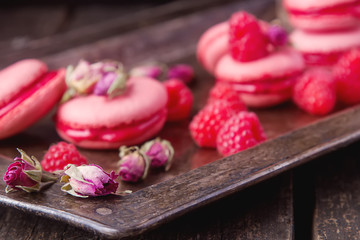 Traditional French sweets. Macaroon with raspberries on a metal tray. Dark wood background.