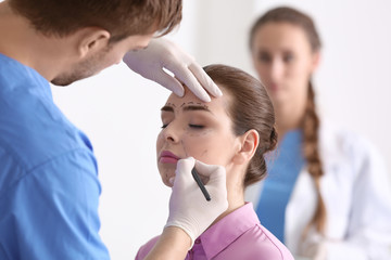Plastic surgeon applying marks onto young woman's face prior to operation