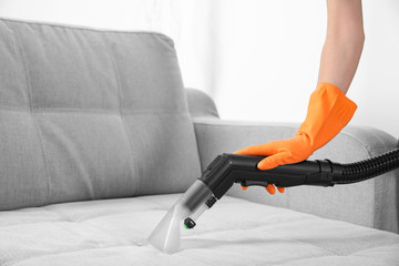 Woman with vacuum cleaner cleaning couch