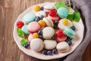 Traditional French sweets. Assorted colorful macaroons with mint green, white and red raspberries, blueberries. Dark wood background. Top view