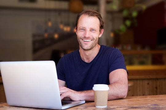attractive man smiling with laptop at cafe