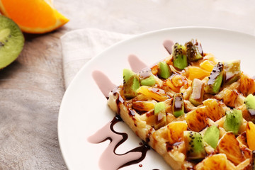 Delicious waffle with fruits and syrup on white plate