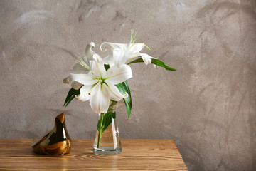 Glass vase with white lilies on wooden table