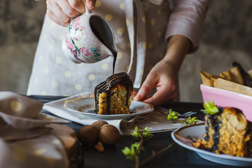 Close-up of the hand of baking girl is pouring chocolate glaze over a mouth-watering piece of cake.