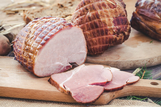 Ham on wooden desk. Rustic background with hay and meat slices.