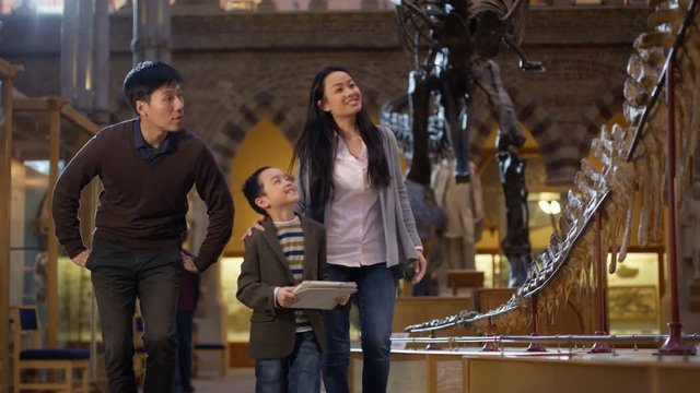  Young Asian family in museum pose to take a selfie with computer tablet