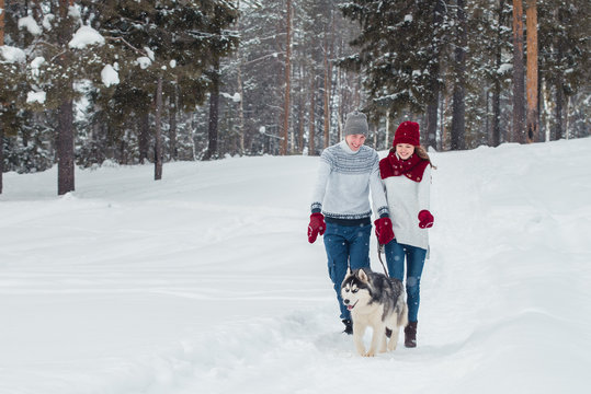 Young couple with a Husky dog walking in winter park, man and woman playing and having fun with dog.