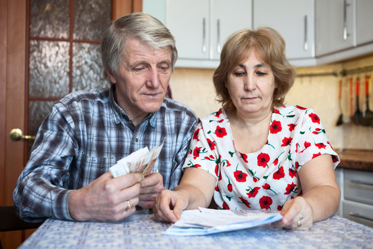 Caucasian elderly couple counts money for communal payments while sitting at the table