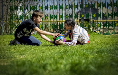 boy and girl playing ball, lying in a meadow