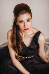 beautiful brunette girl with red lips in long black dress sitting on the floor looking at the camera bottom-up close-up portrait