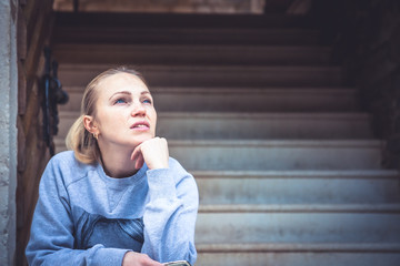 Thinking young woman sitting on stairs and look up with copy space. Concept for forecasting and way...