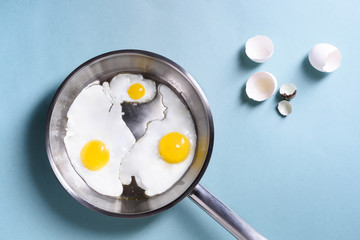 Healthy morning breakfast with fried eggs, over a blue table background. Chicken egg and quail egg in a pan. Top view, copy space, flat lay.