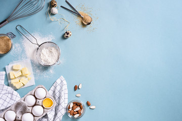 Healthy baking ingredients - flour, almond nuts, butter, eggs, biscuits over a blue table...