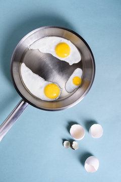 Fried eggs for breakfast in a cooking pan. Chicken egg, quail egg, yolk and egg shell. Top view, copy space. Flat lay.
