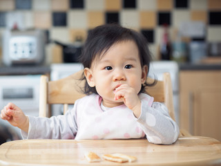 Asian baby girl eating toasted at home kitchen