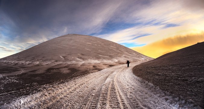 I colori del tramonto del paesaggio innevato sul vulcano Etna con escursionista su sentiero