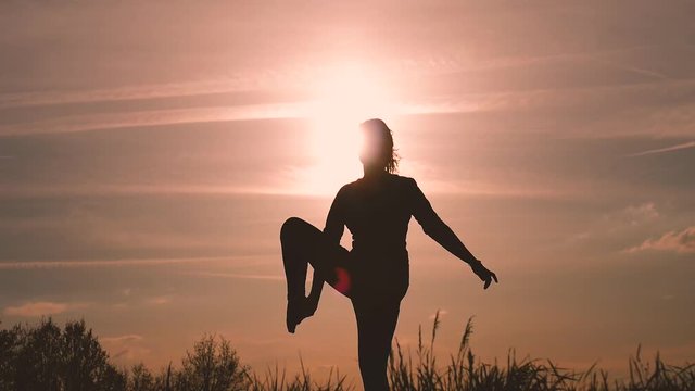 silhouette of a girl performs some dance poses in backlight during sunset in the countryside to train and take care of herself