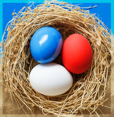 Red, blue, white eggs ( As flag of some countries ) in nest on rustic wooden background, selective focus image. Happy Easter Card - space for text. 