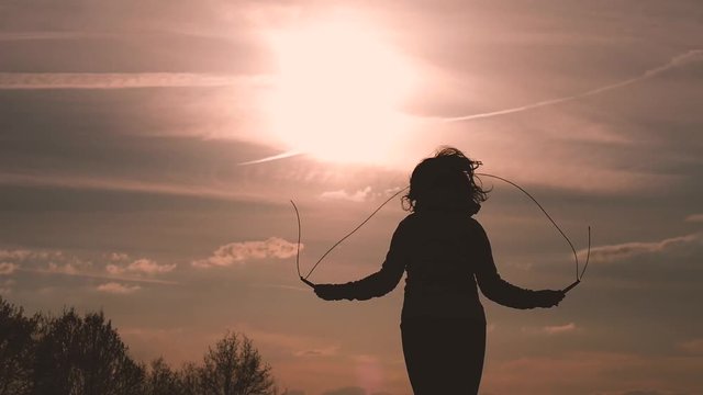 silhouette of a girl jumping rope for training during sunset in backlight on campaign
