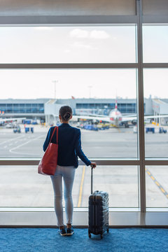 Silhouette of woman waiting at airport terminal for flight boarding. Businesswoman traveling looking through the window at tarmac and planes. Business travel concept.