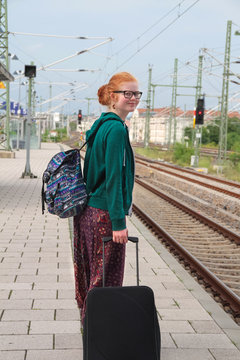 Jugendliche mit Koffer und Rucksack wartet am Bahnsteig auf Zug