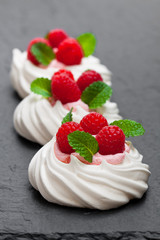 Mini  Pavlova meringue nests with raspberries and mint on black stone background