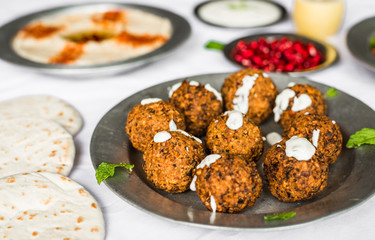 Crispy falafel, Arab pita bread, tabbouleh salad, with pomegranate seeds and white sour cream sauce against white background. Selective focus.