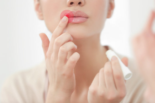 Woman applying hygienic lip balm near mirror