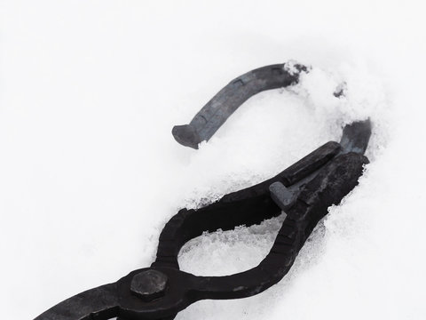 Forge, handmade: tongs for hot forging with horseshoe. Cooling the red-hot horseshoe in the melts snow - Powered by Adobe
