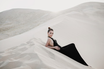 Beautiful sexy asian woman in a black dress on a dune of desert