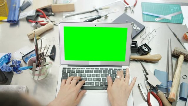  Jewelry designer at workbench working on computer with green screen. Close up on hands, no faces. 