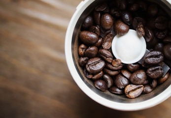 Electric coffee mill machine with fresh coffee beans inside. Coffee grinder on a brown wooden table in the kitchen.