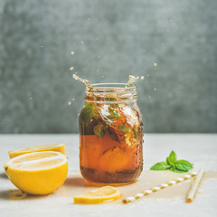 Summer cold Iced tea with fresh bergamot, mint and lemon in glass jar with splashes on light table,...