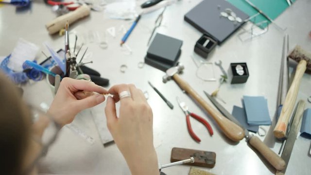 Overhead view looking down jewelry designer at workbench with tools, materials and jewelry items