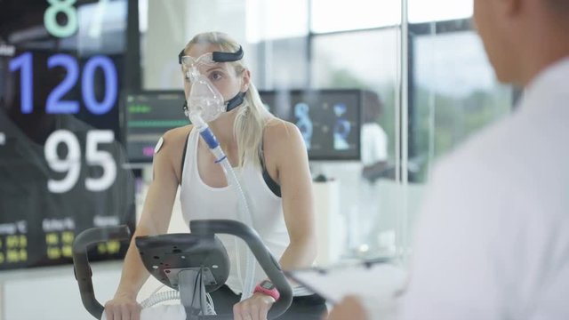  Female athlete on exercise bike being tested and monitored by sports scientist. 