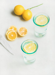 Morning detox lemon water in glasses served with fresh lemon fruits over light grey marble background, selective focus. Clean eating, weight loss, healthy, detox, dieting concept