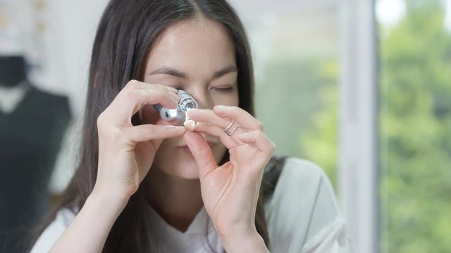  Jewelry maker in her studio looking through a loupe to check quality of ring. 