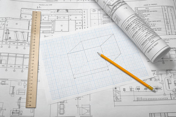 A set of open and rolled up blueprints on wooden table background with a pencil and a ruler lying beside.
