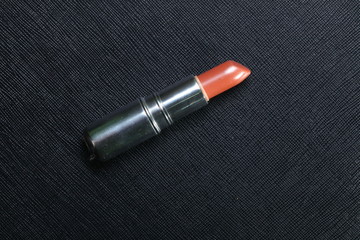 Lipstick earth tone color reflection  from studio light put on the black color leather surface as a background represent the beauty cosmetic accessory.