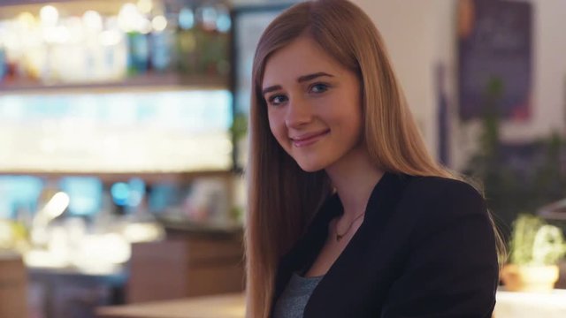 Happy cute girl in the black jacket is sitting in the café. She is focused on the work with her notebook.