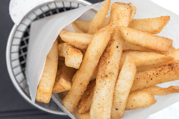 Potatoes fries in a little white paper bag on wood board